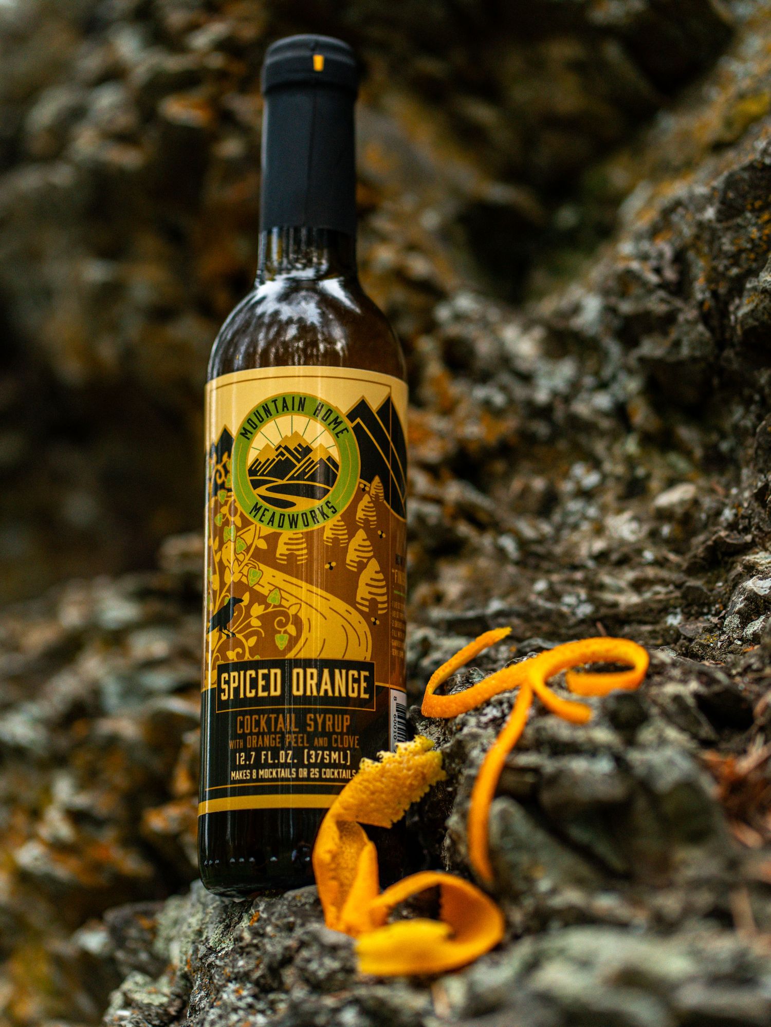 Bottle of spiced orange liqueur alongside curled orange peel garnish against a textured stone background.