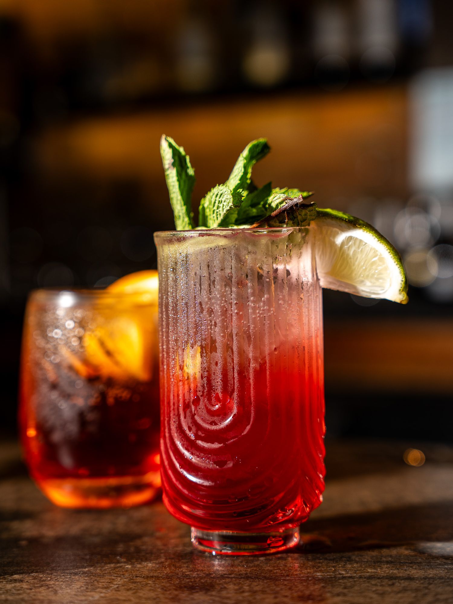 Red gradient cocktail in an etched glass garnished with mint leaves and lime wedge.