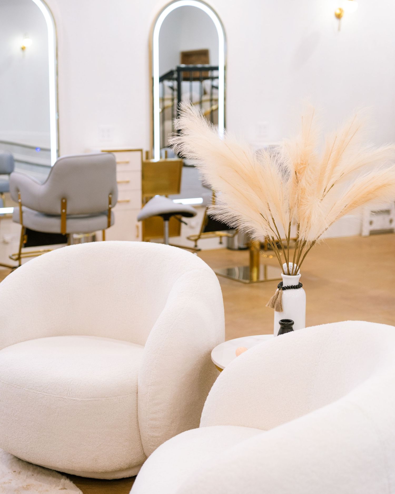 Elegant spa waiting area with curved white chairs and pampas grass decor.