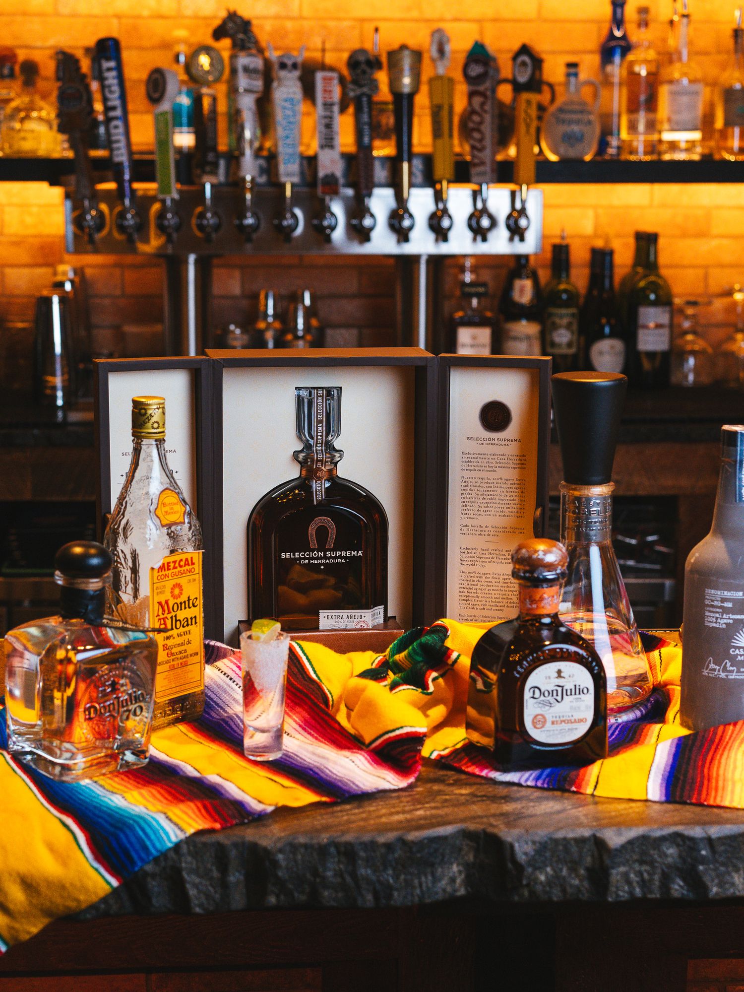Bar display with various liquor bottles arranged on colorful Mexican serape blanket.