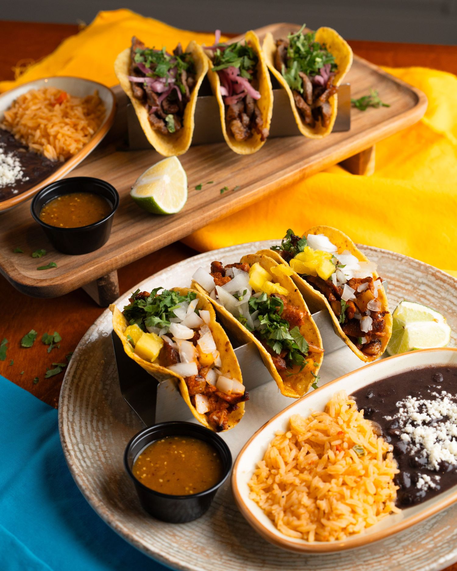 Rustic wooden board presenting tacos with rice and black beans, served with salsa dipping sauce and fresh garnishes.