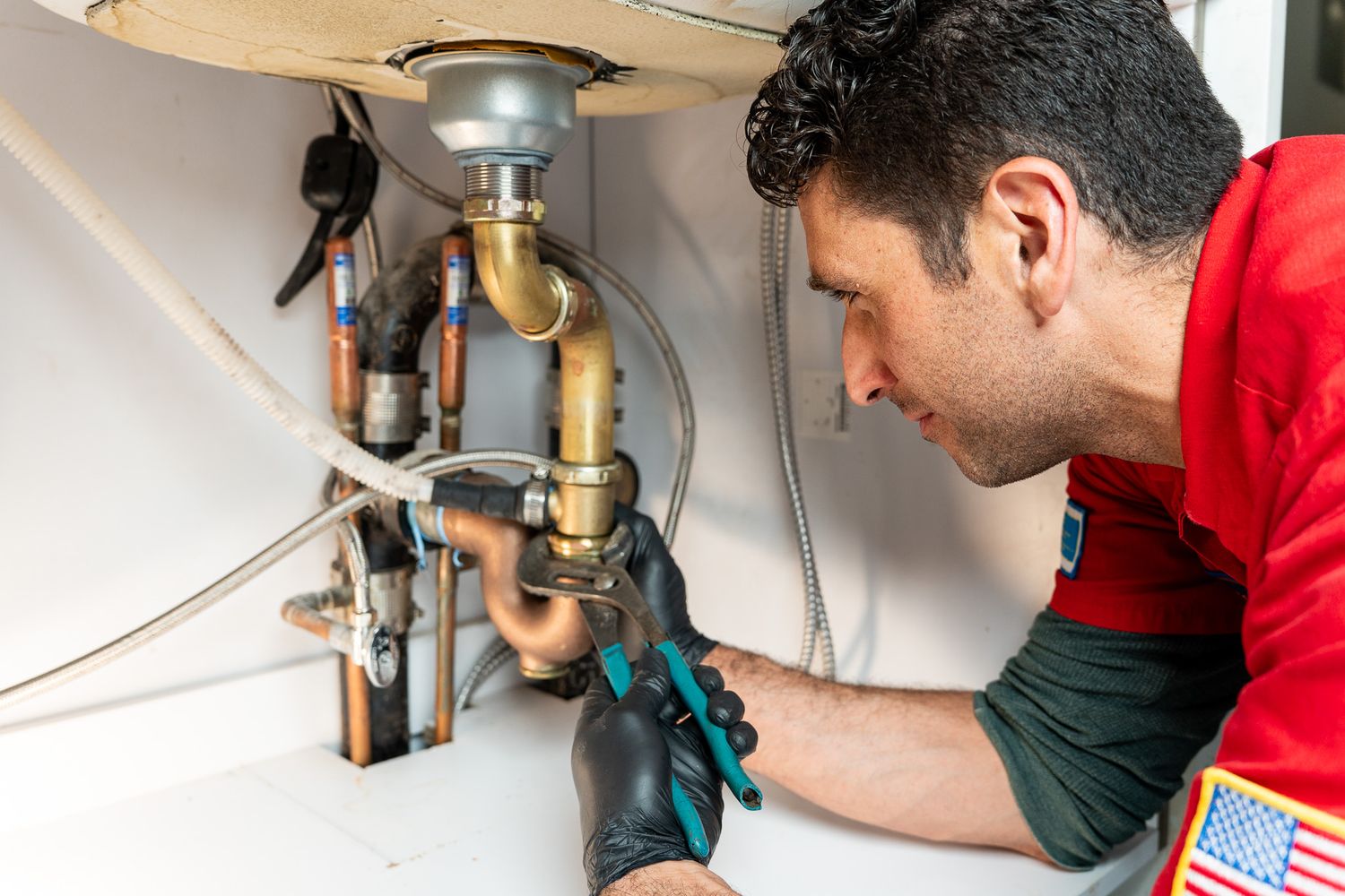 Plumber working on sink pipes underneath bathroom cabinet.