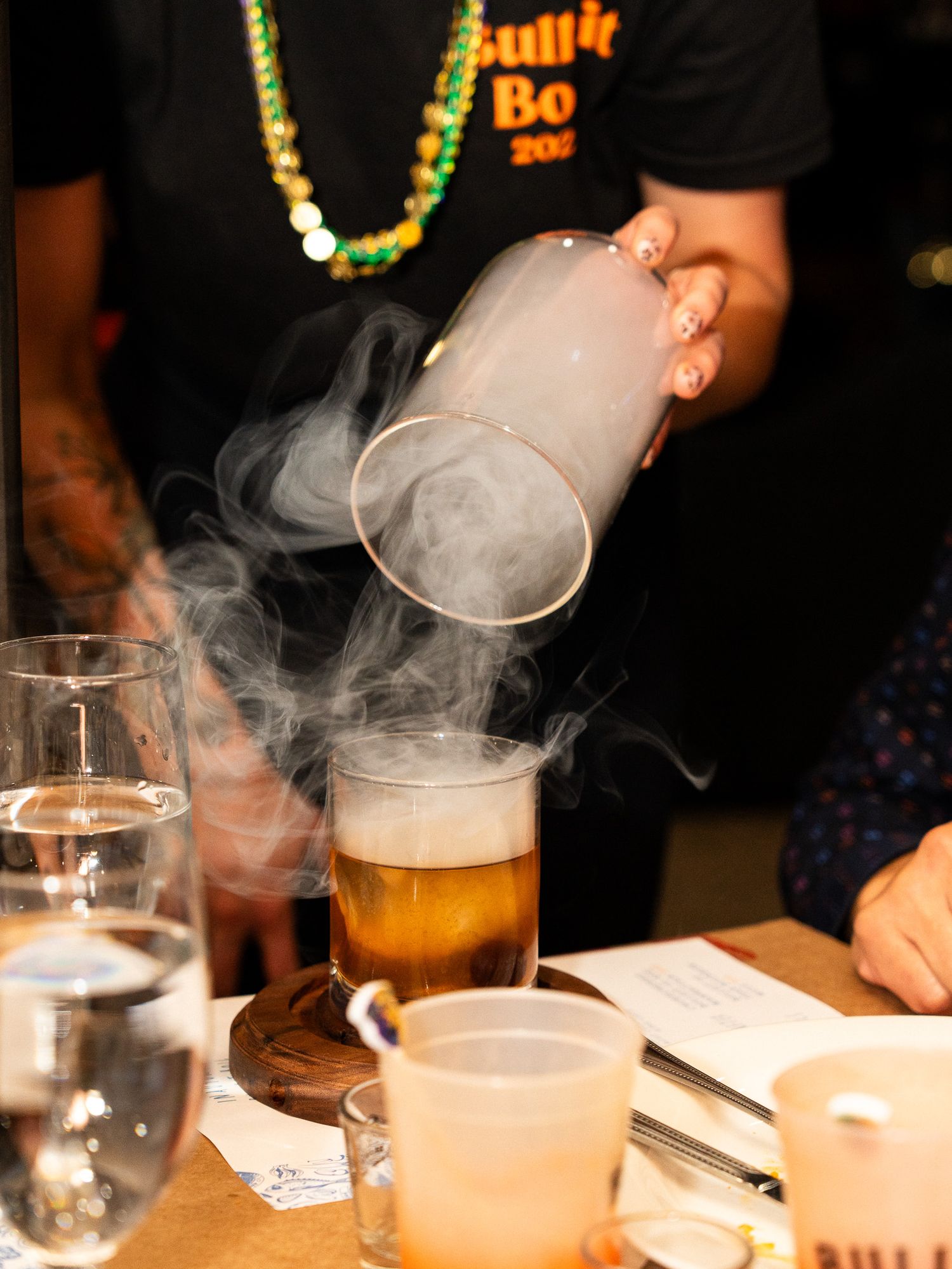 Smoke rises from a craft cocktail being poured at a bar event.