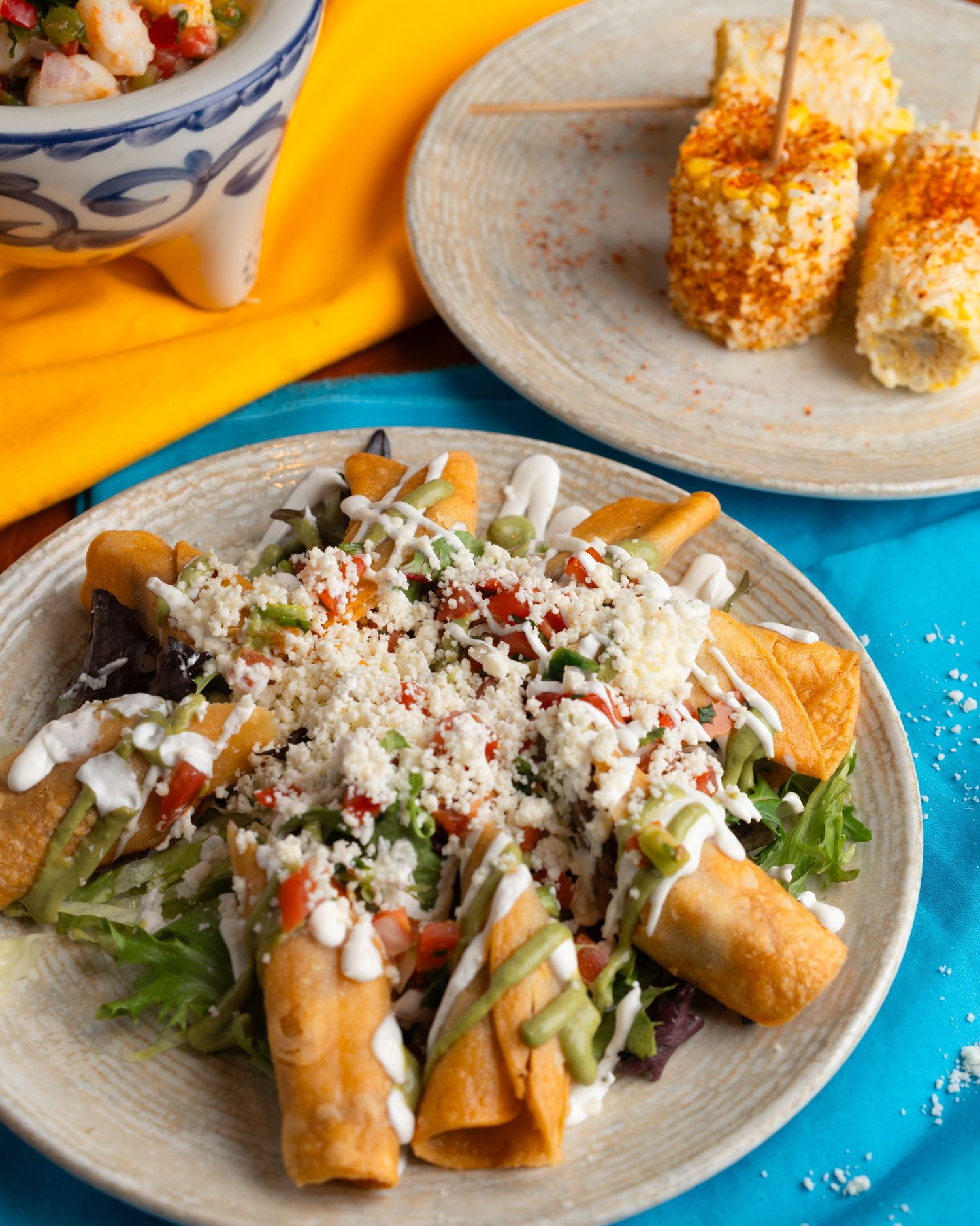 Crispy taquitos topped with shredded lettuce, cheese, and cream sauce served on a rustic ceramic plate.