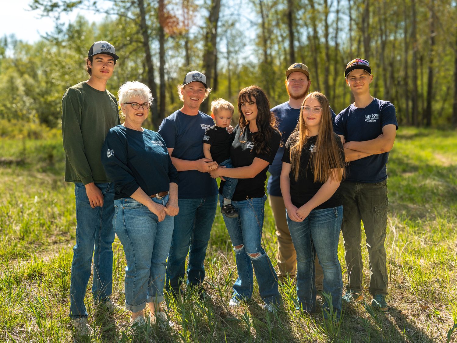 Group of people in matching navy shirts pose together outdoors in natural setting.