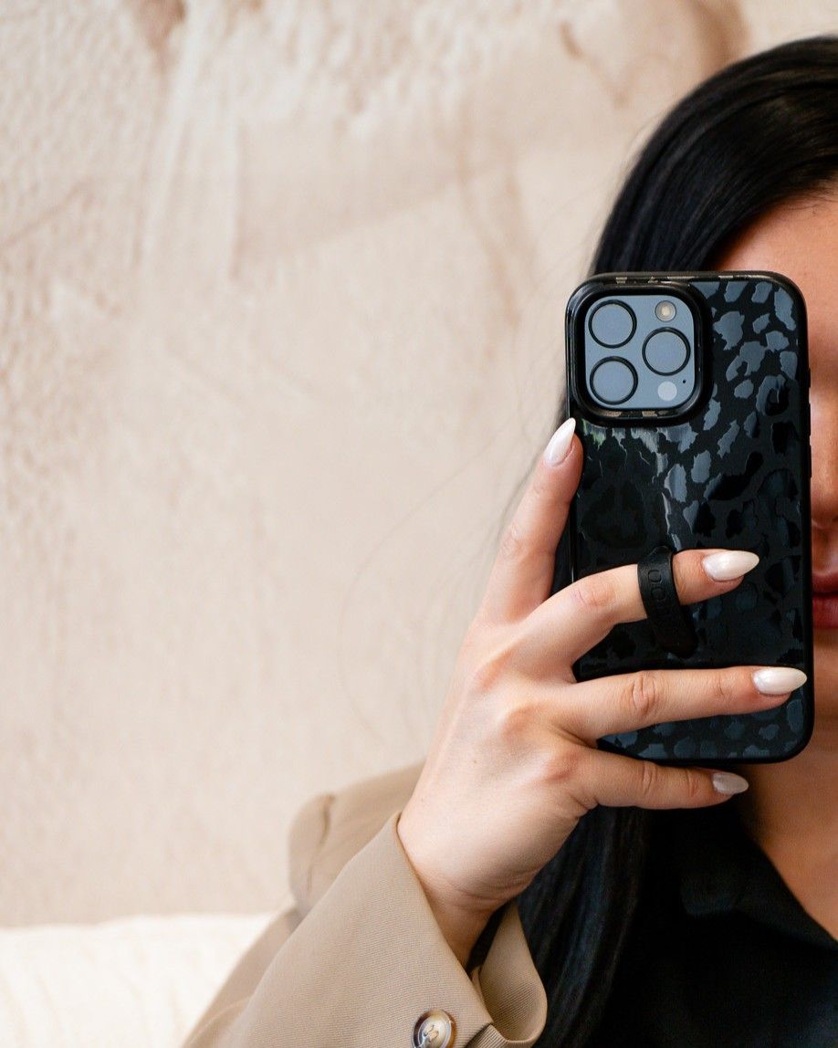 Close-up of hands holding black textured iPhone case against beige wall.