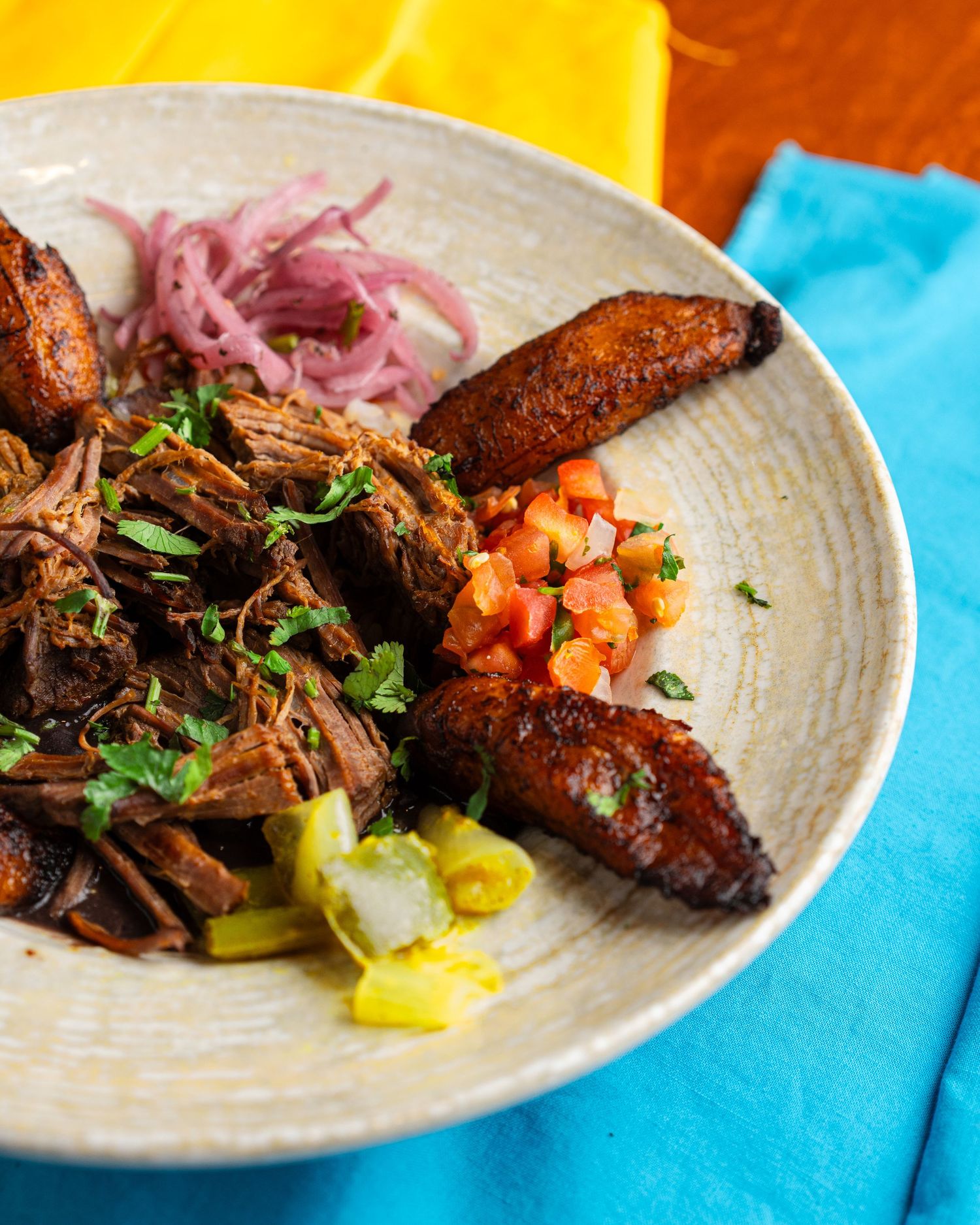 Braised meat dish with pickled onions and plantains served on a textured ceramic plate.