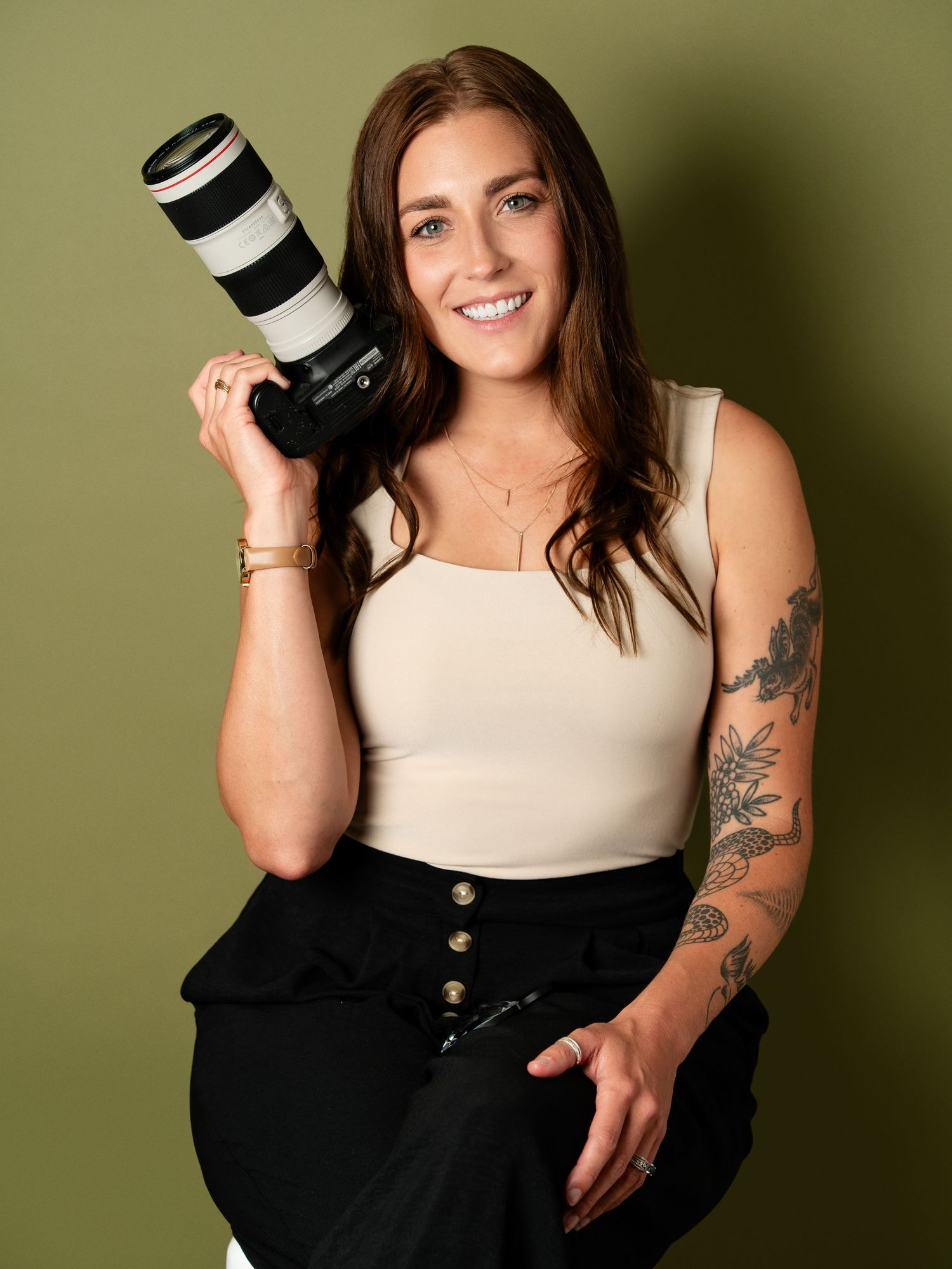 A photographer holding professional camera with striped lens against olive green background.