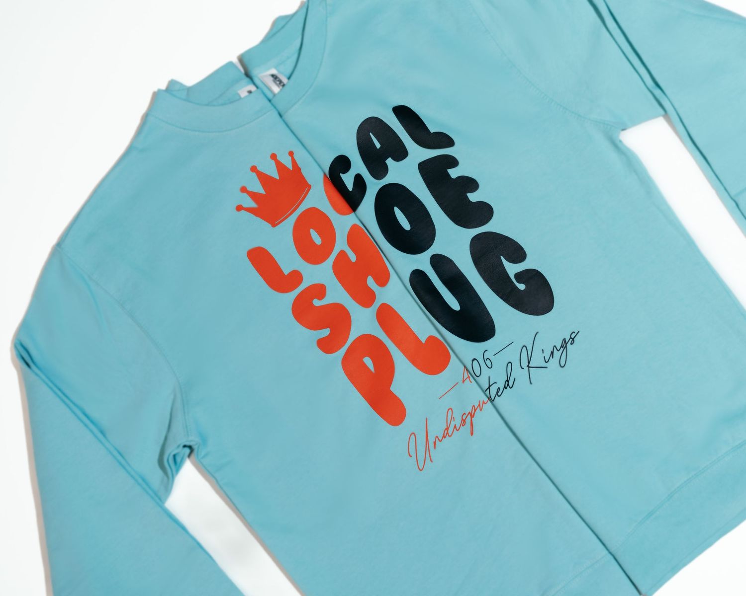 Light blue sweatshirts with black and orange text graphics laid flat.