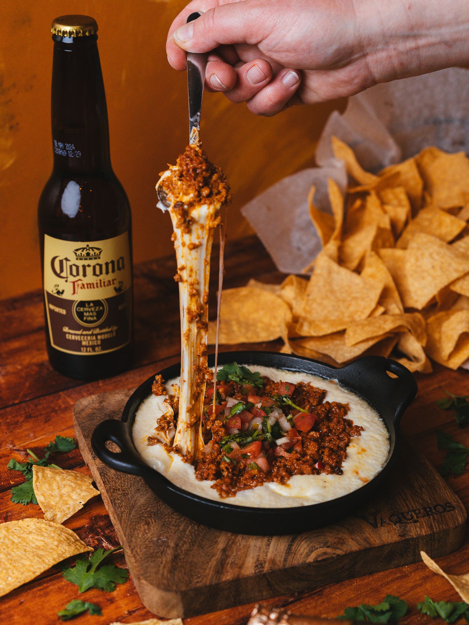 Queso fundido with tortilla chips and Corona beer on a rustic wooden table.