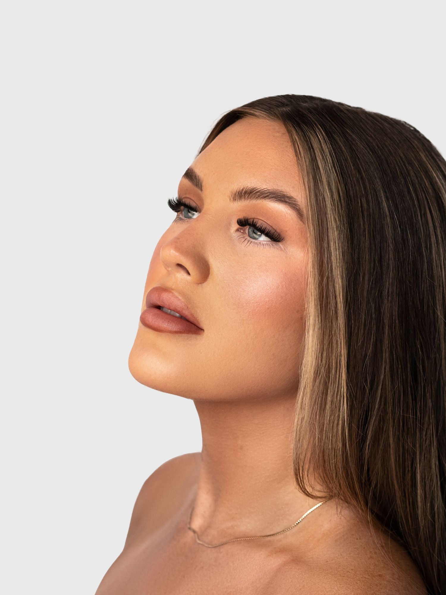 Profile view beauty portrait highlighting glowing skin and elegant neckline jewelry.