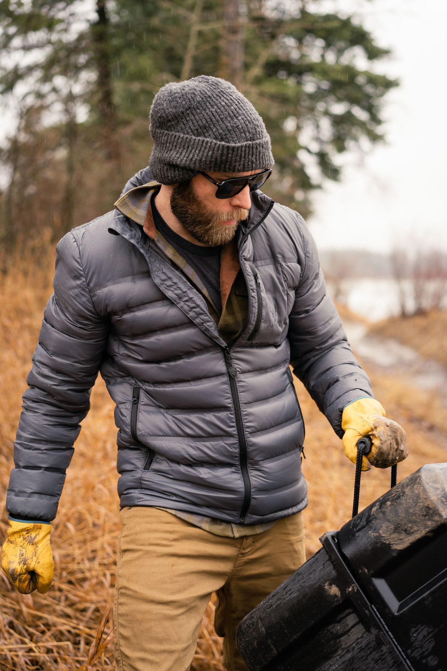 Person wearing gray puffer jacket and tan pants works outdoors on autumn day.