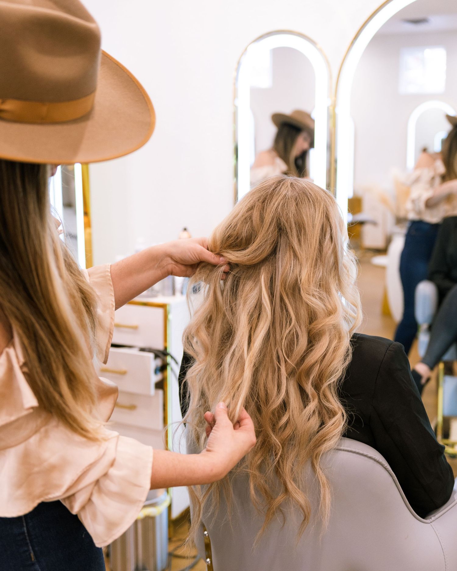Close-up of hairstylist styling blonde wavy hair in salon.