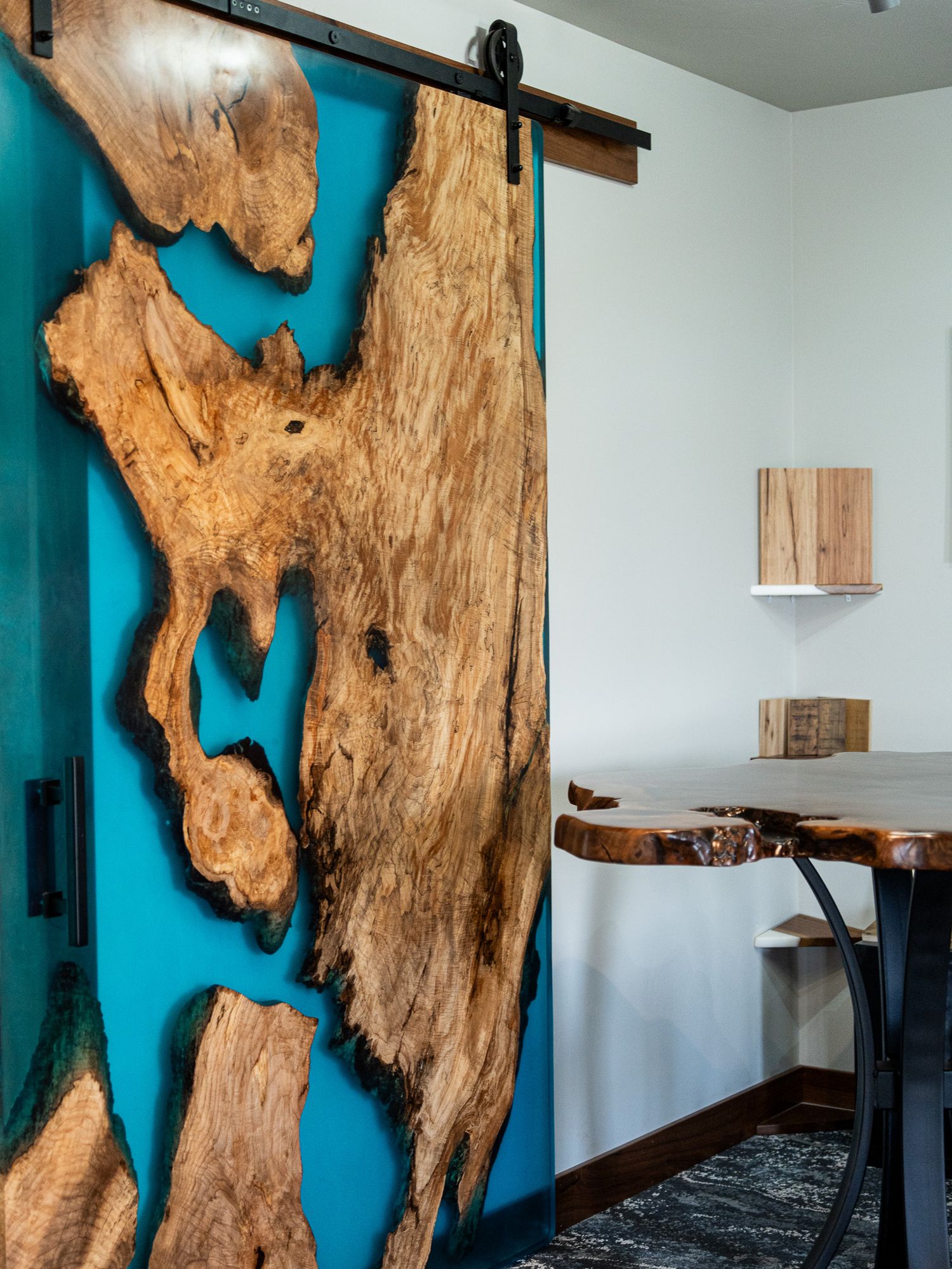 A rustic sliding barn door features natural wood with turquoise resin inlay, paired with matching floating shelves nearby.