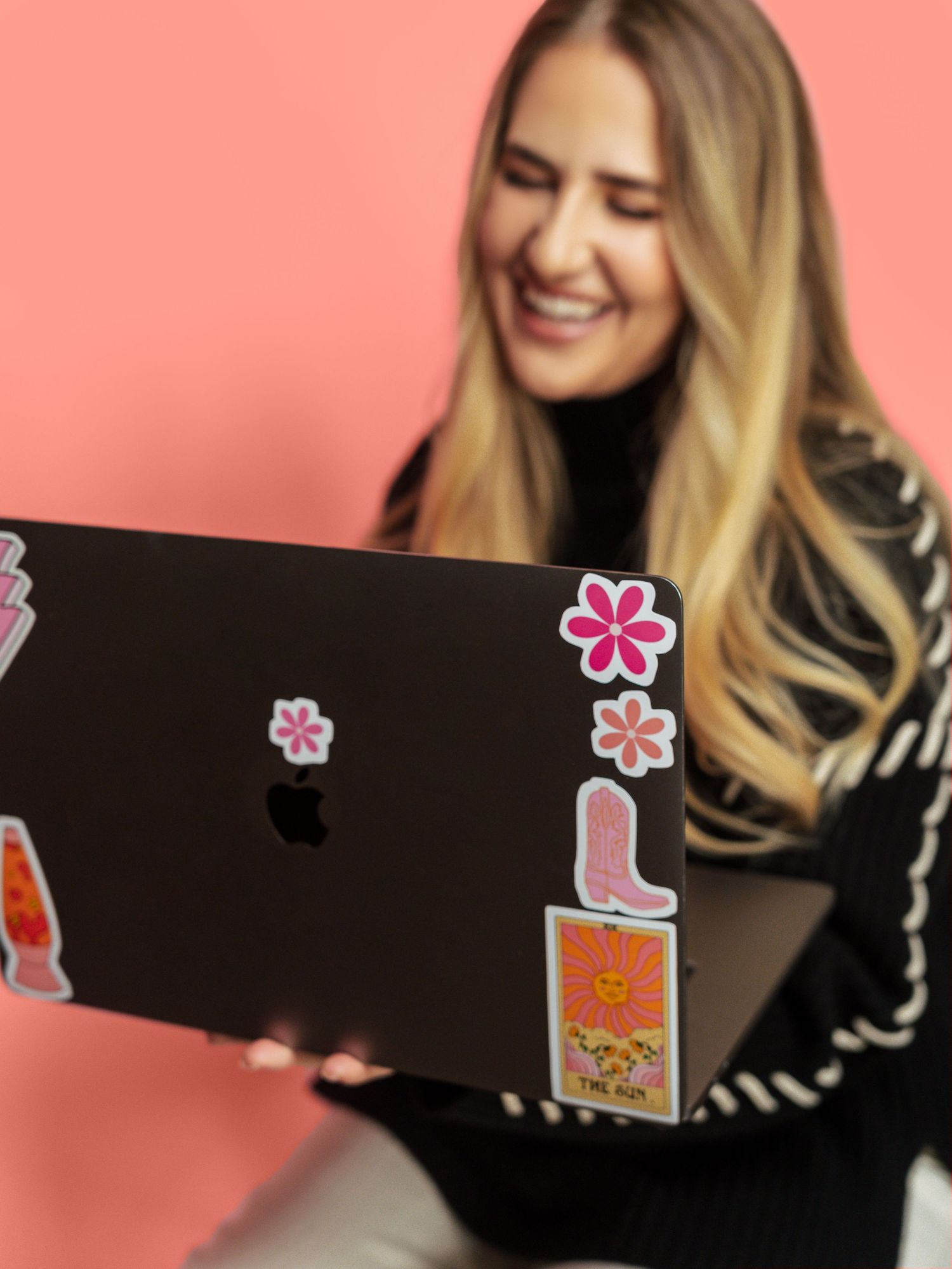 Person using laptop decorated with flower stickers against pink background.