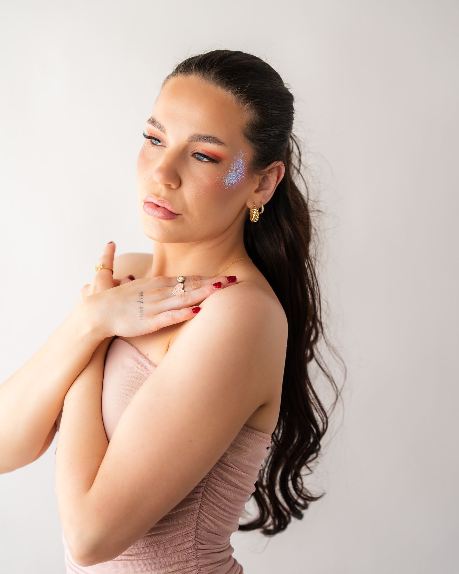 Portrait of woman with glitter makeup and long dark hair against white background.