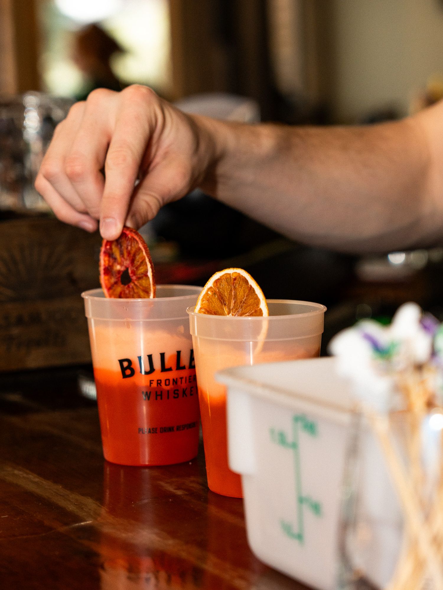 Hand garnishing an orange cocktail with dried citrus slice in a plastic cup.
