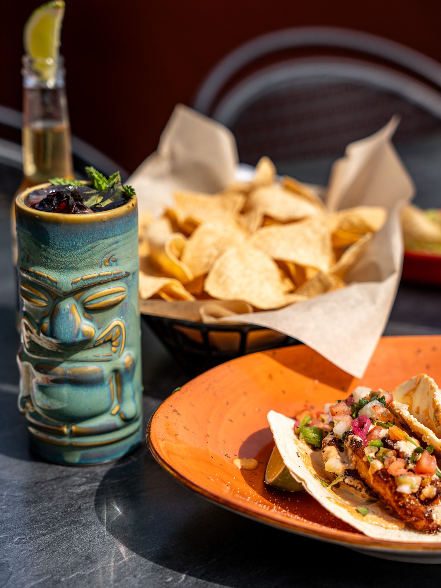 Tiki cocktail glass and tacos served with tortilla chips on orange plate at Mexican restaurant.
