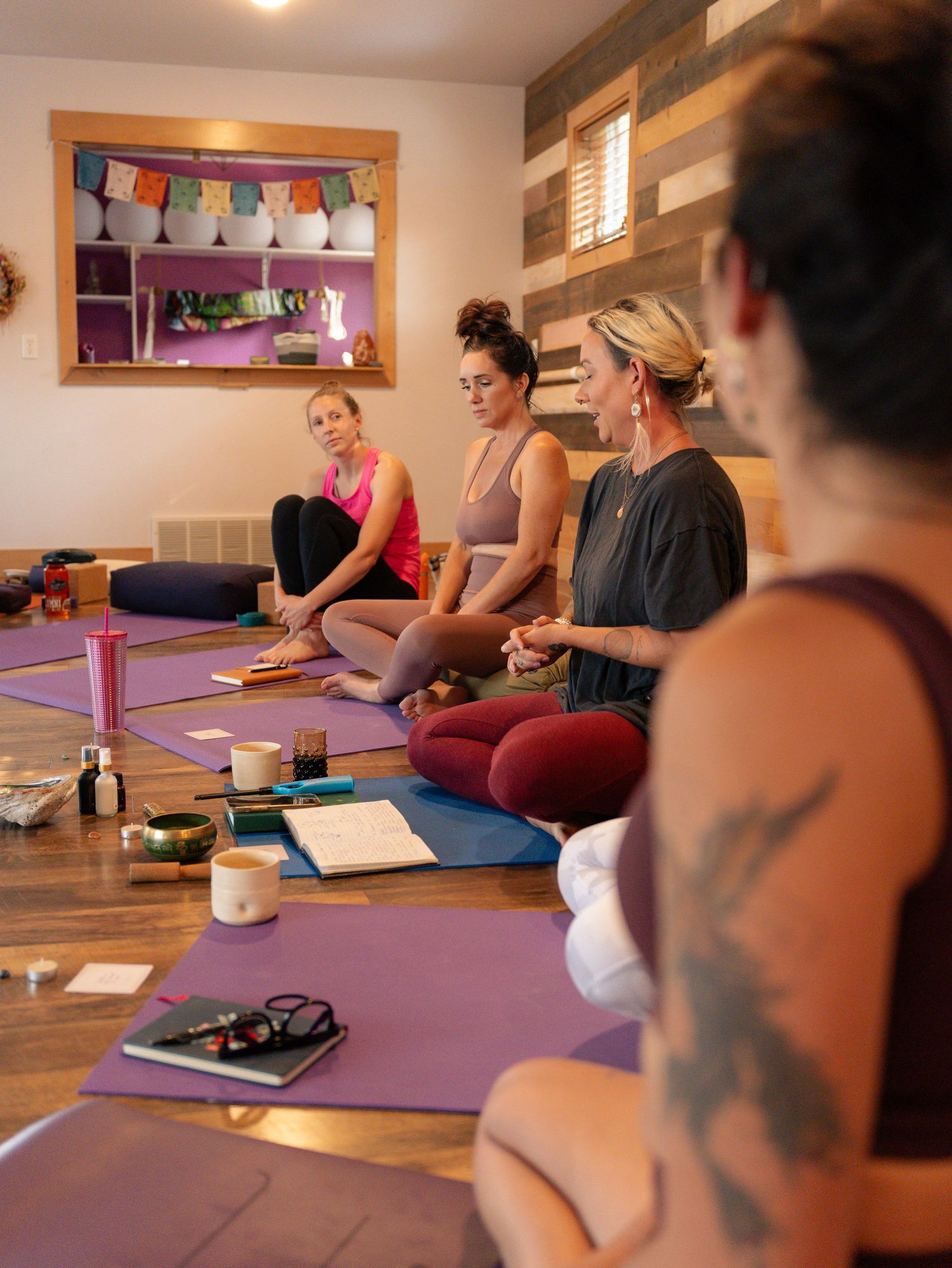 Group meditation session with purple yoga mats and wellness accessories on wooden floor.