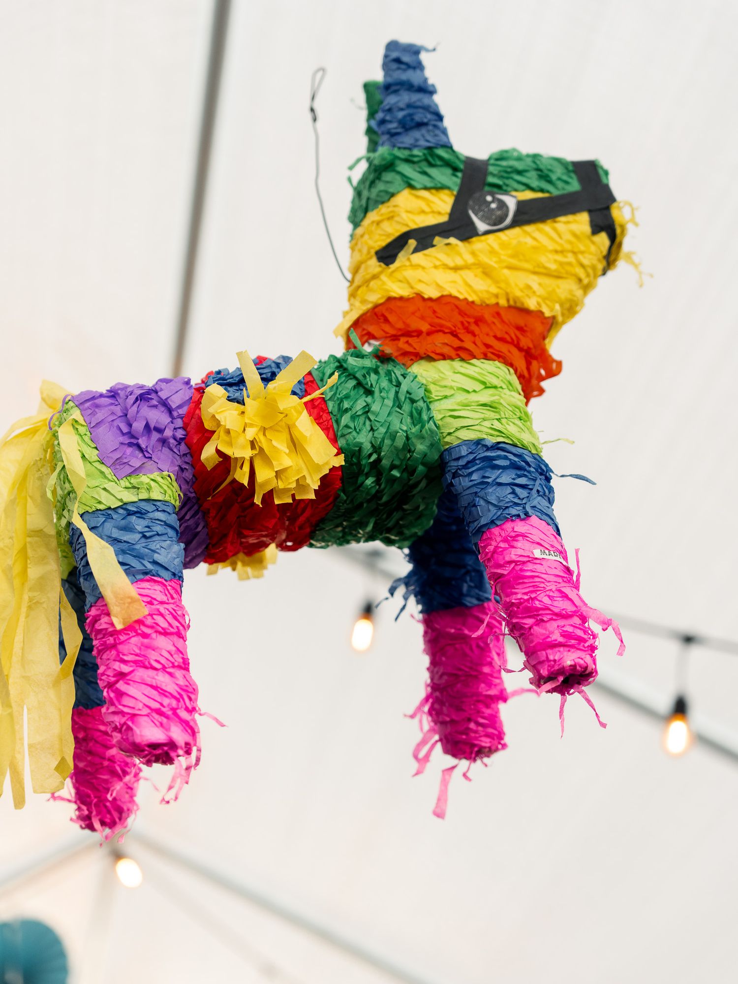 Colorful Mexican-style paper pinatas hanging from string lights with vibrant rainbow patterns.