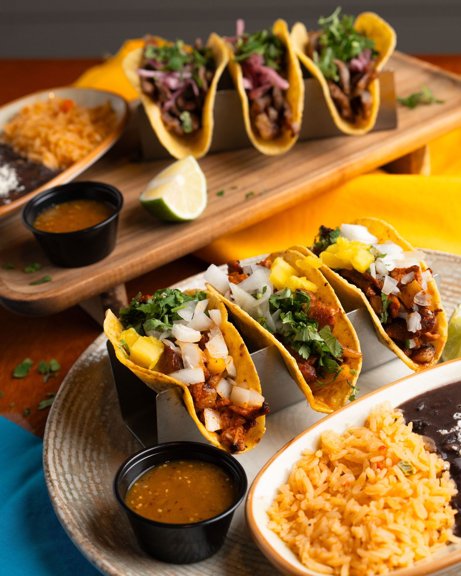 Authentic Mexican tacos served on wooden board with rice and dipping sauce.