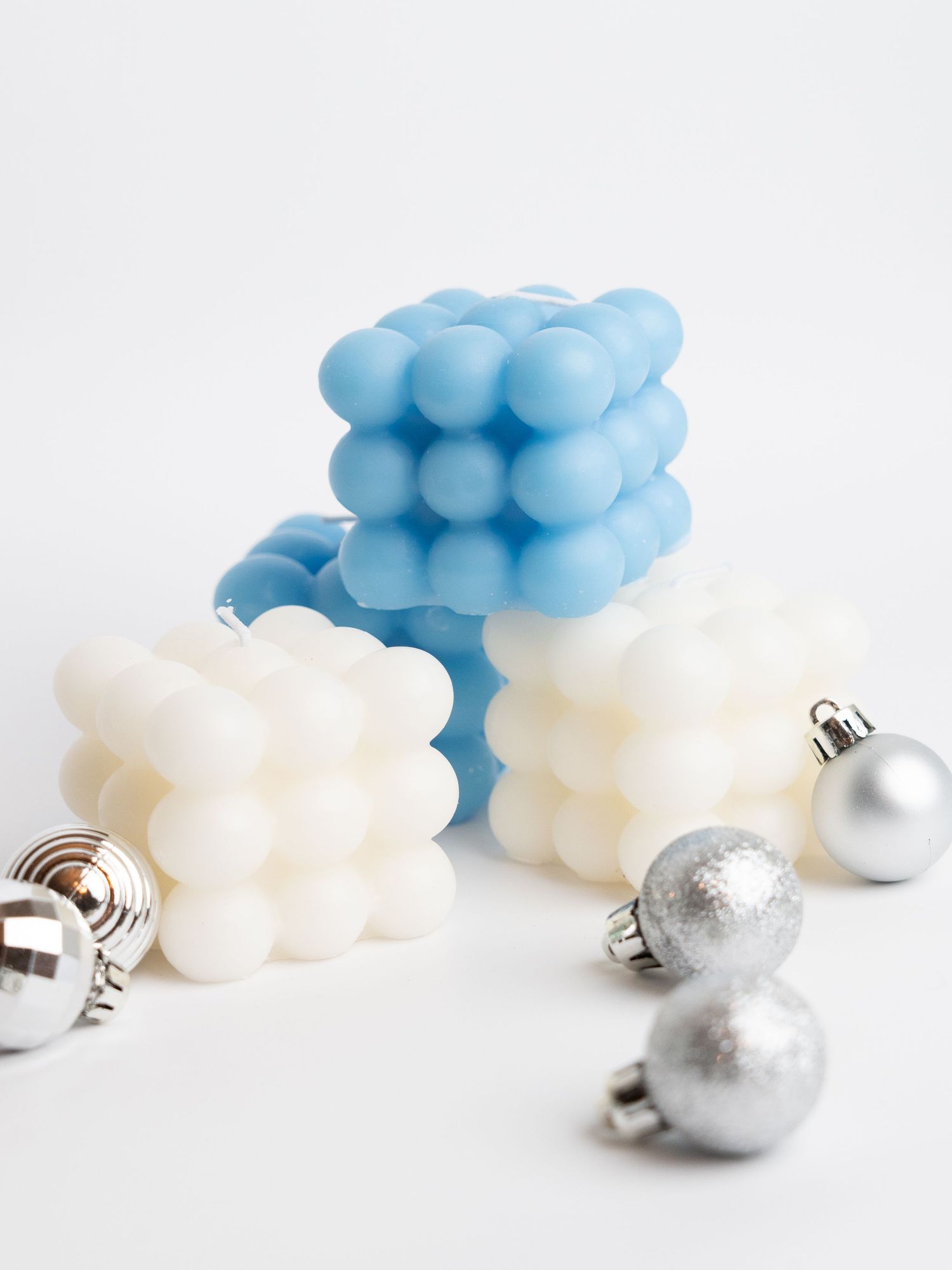 Blue and white bubble cube candles arranged with silver Christmas ornaments on white surface.