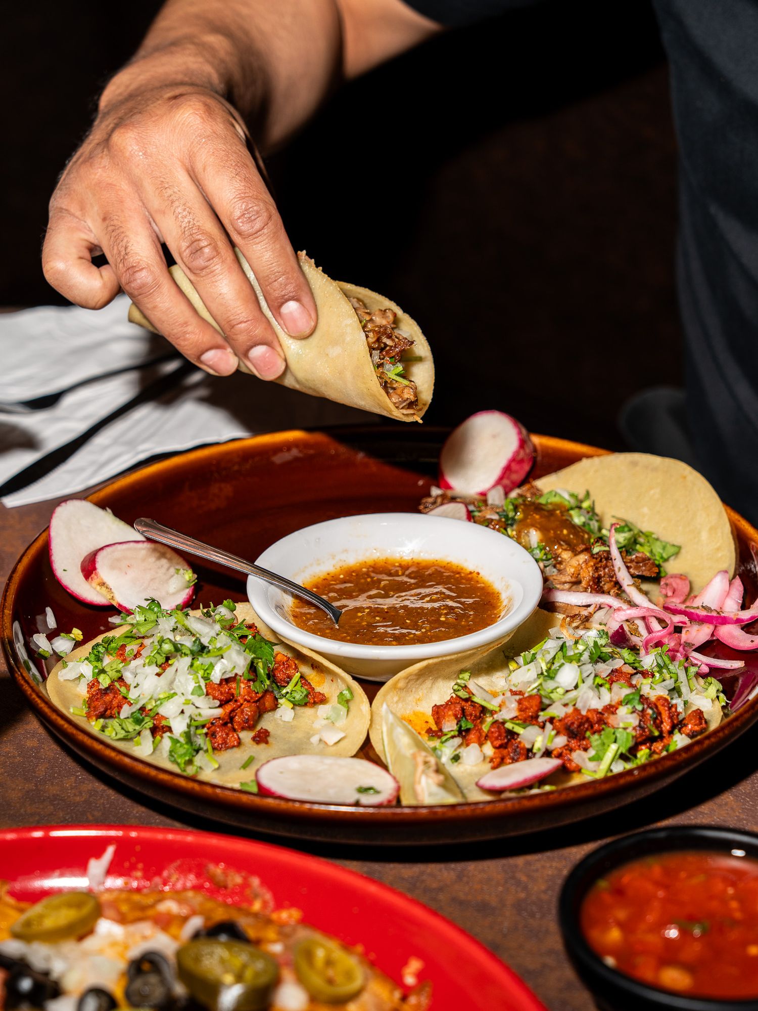 Street-style tacos on a round platter with garnishes and dipping sauce in the center.
