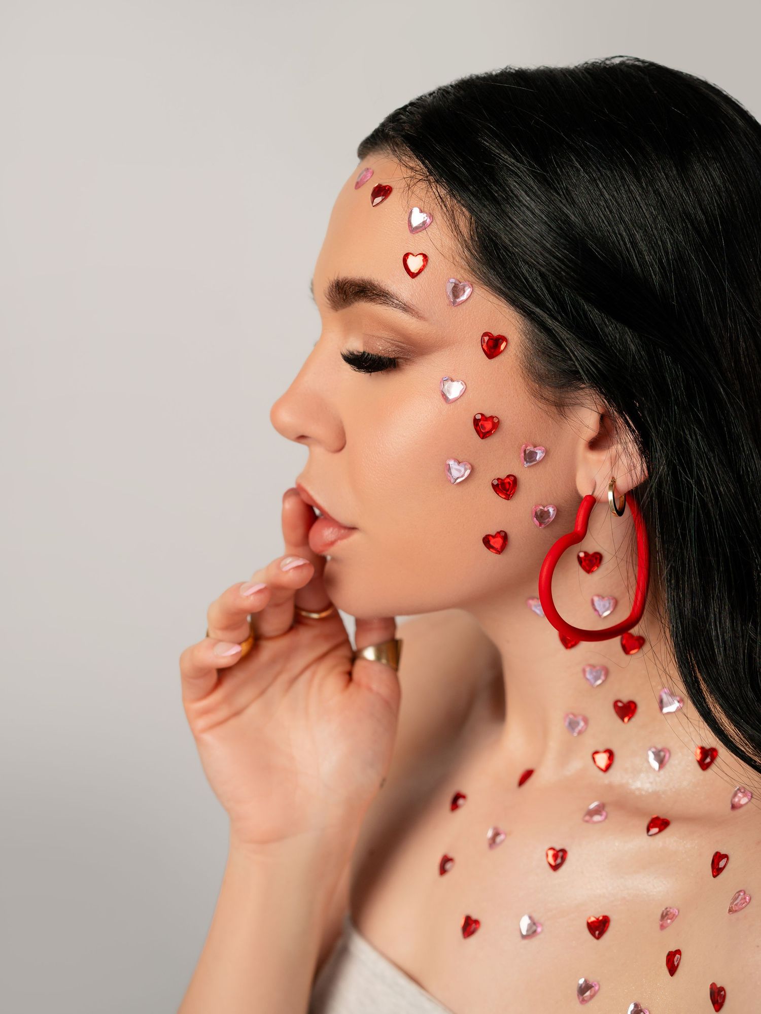 Artistic beauty shot featuring decorative heart gems and red earrings against white background.