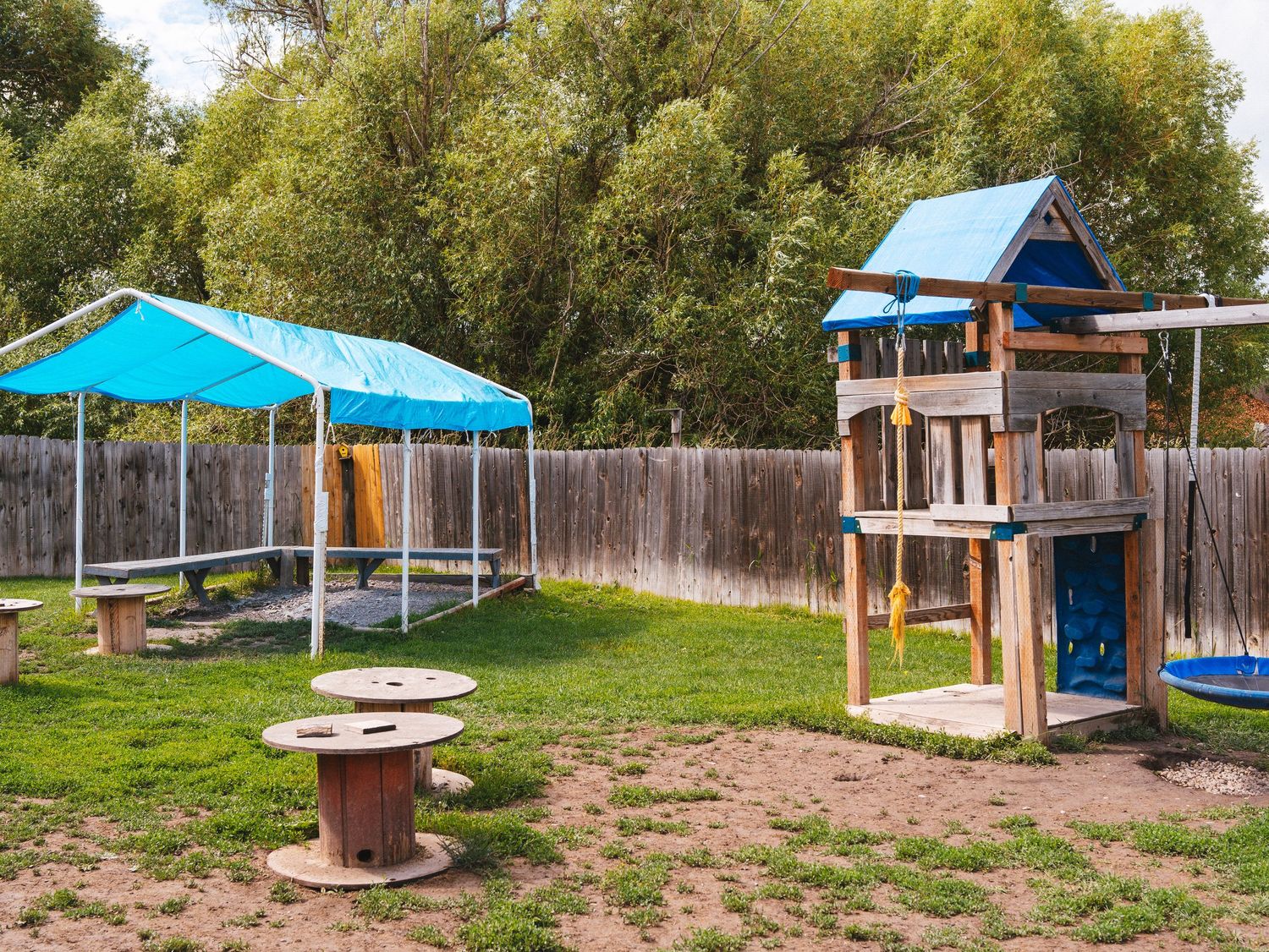 Outdoor playground featuring a blue wooden playhouse and turquoise canopy in a fenced yard.