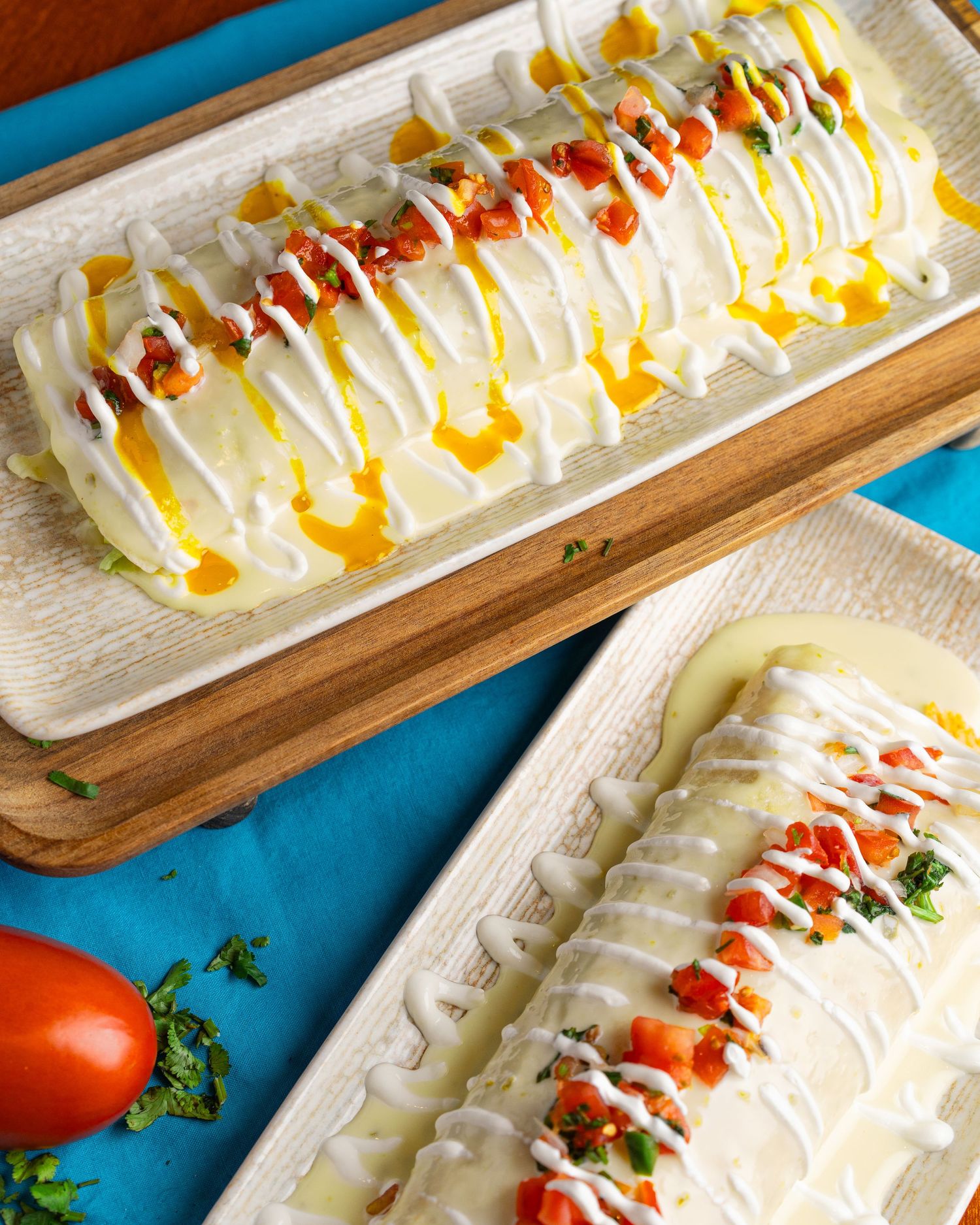 Long white platter of sushi rolls drizzled with spicy mayo and eel sauce on a wooden serving board.