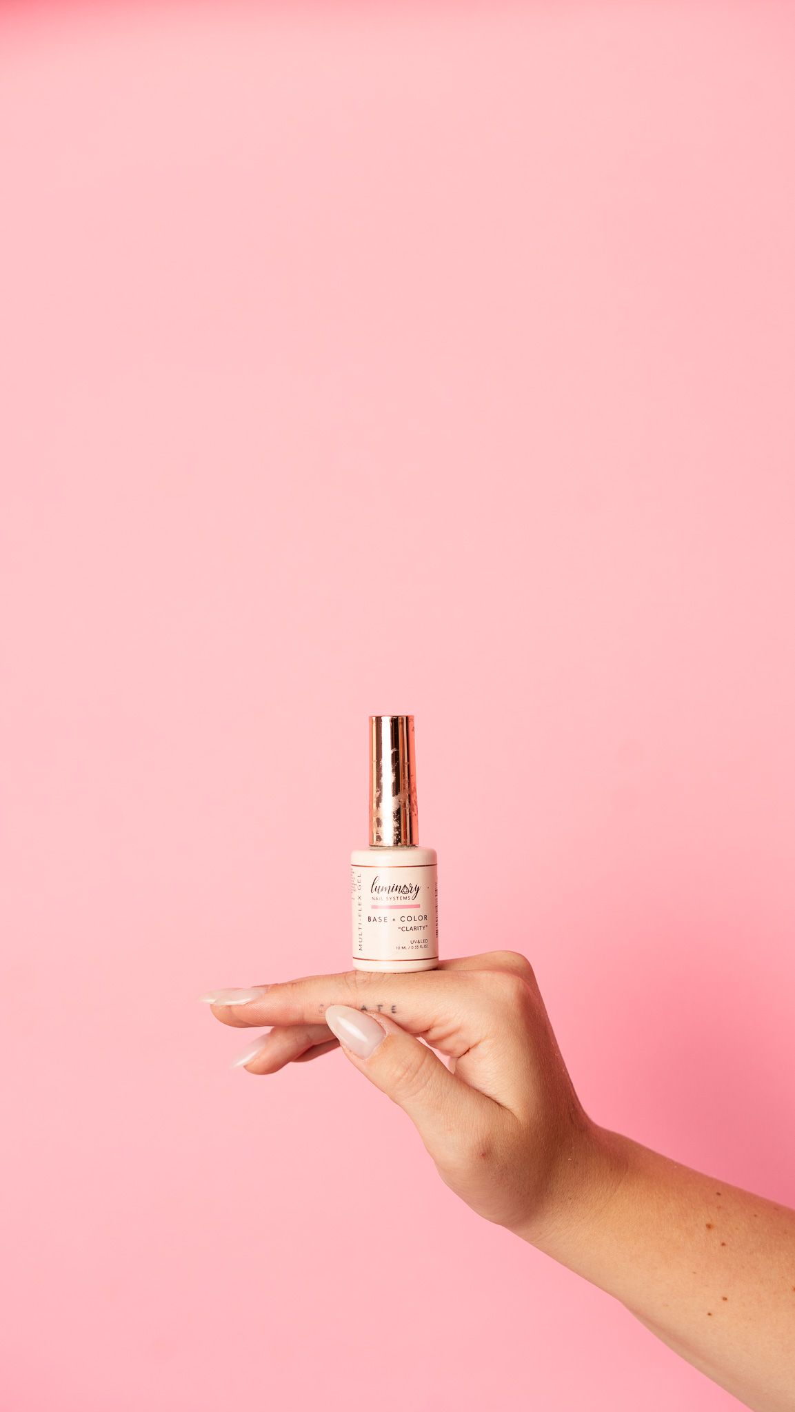 Hand holding a small glass bottle against pink background.