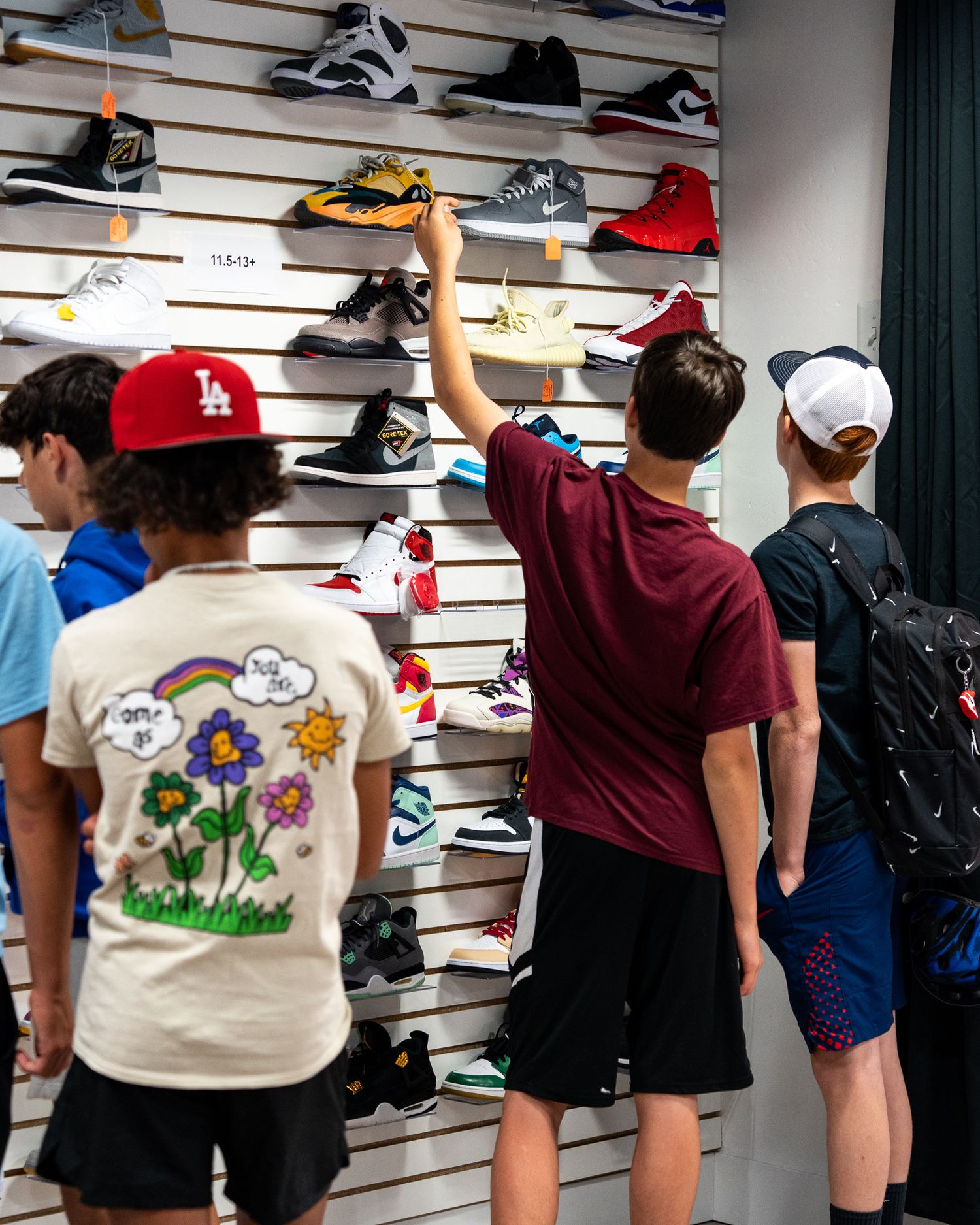 Customers browsing wall display of sneakers at a shoe store.