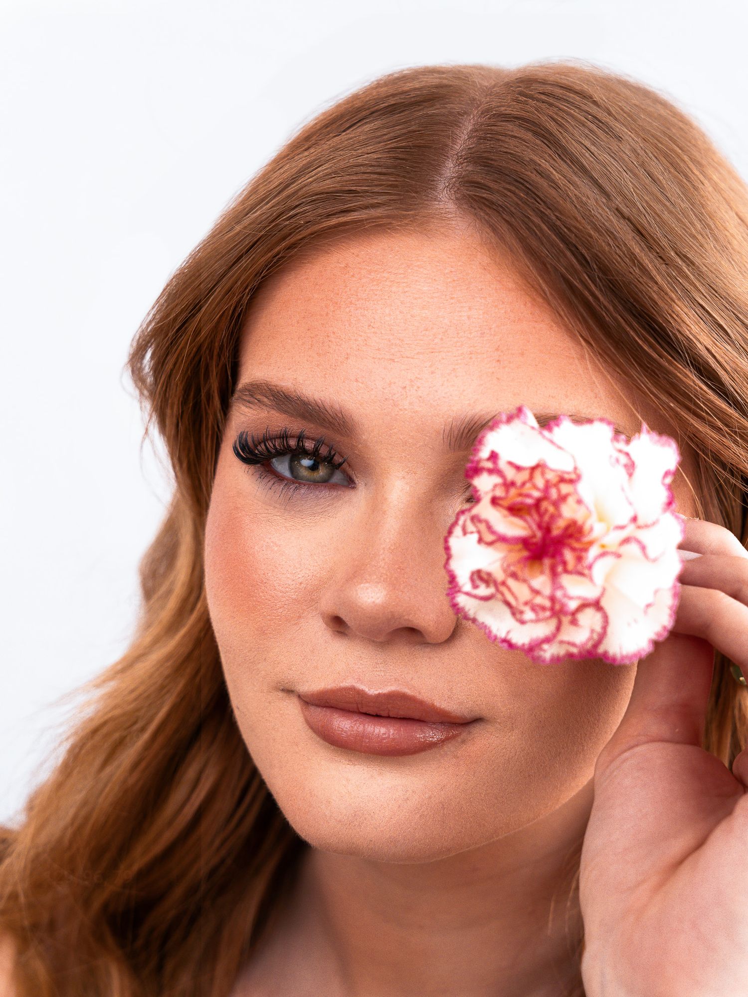 Creative beauty shot with pink carnation flower accent and neutral makeup tones.