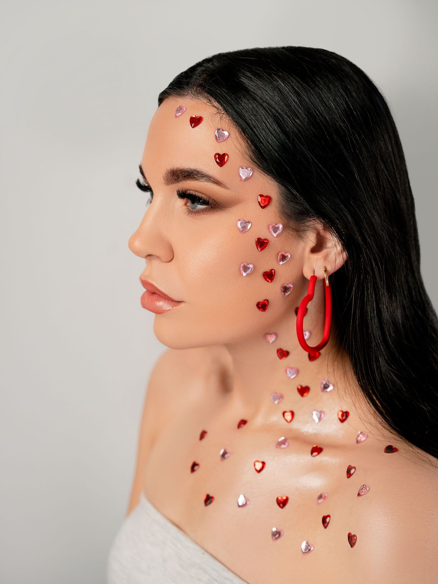 Creative beauty portrait with red heart-shaped rhinestone gems applied to face and neck.