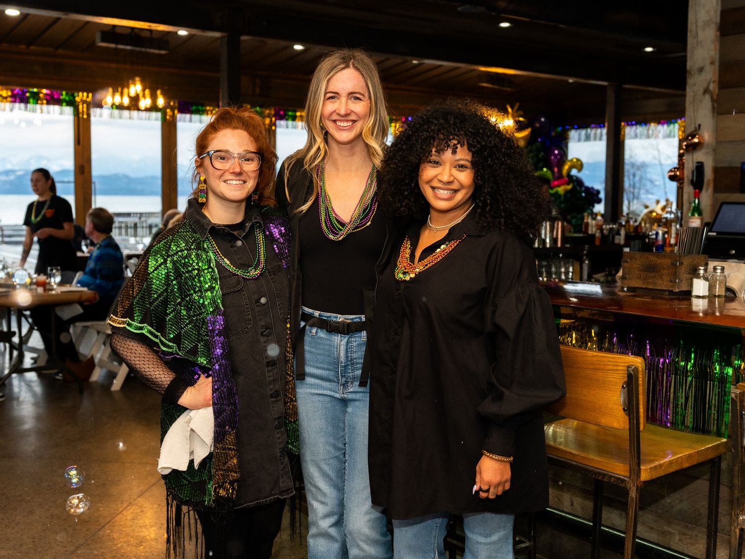Three friends sharing a fun moment together at a restaurant with ocean views in the background.