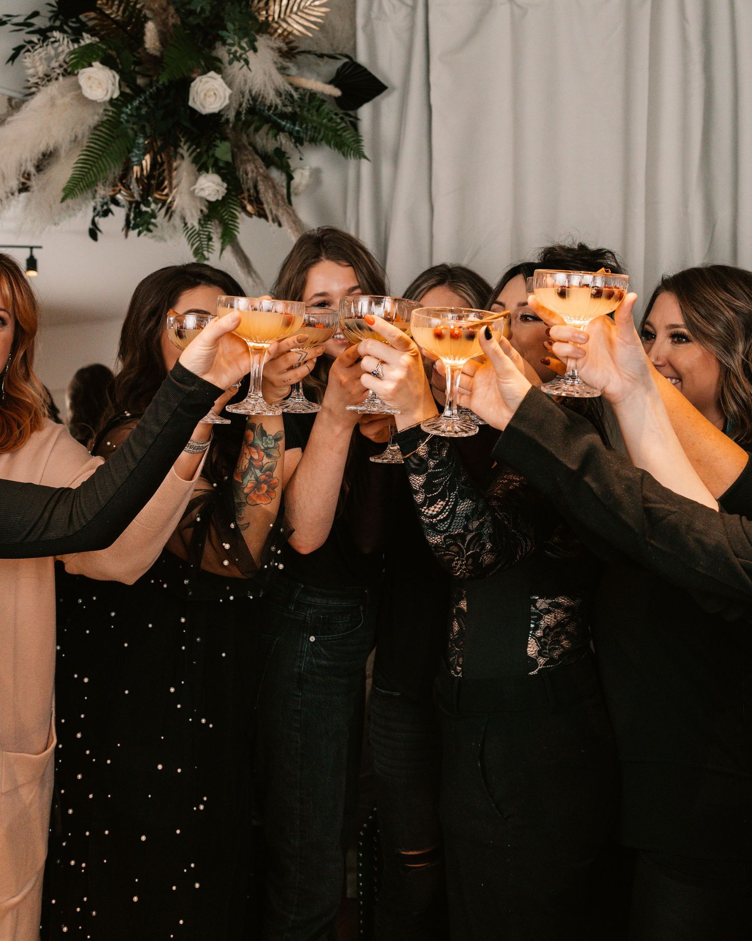 A group is positioned in a row raising champagne glasses in celebration with evergreen decor visible above them.