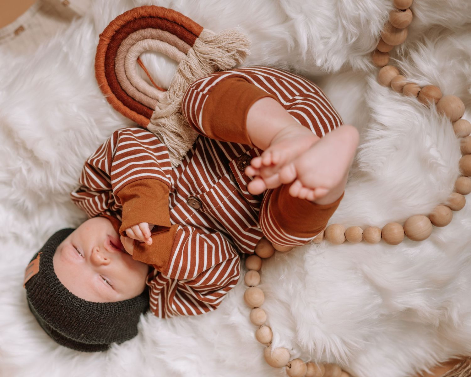 Baby lying on white fluffy rug wearing striped brown outfit.