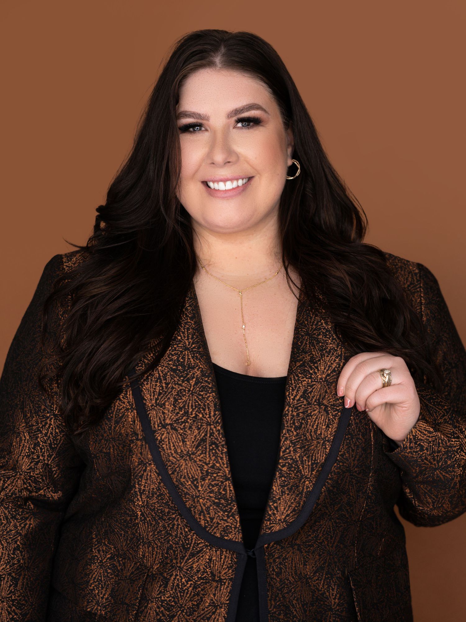 Portrait series in black top and brown lace jacket against warm brown background.
