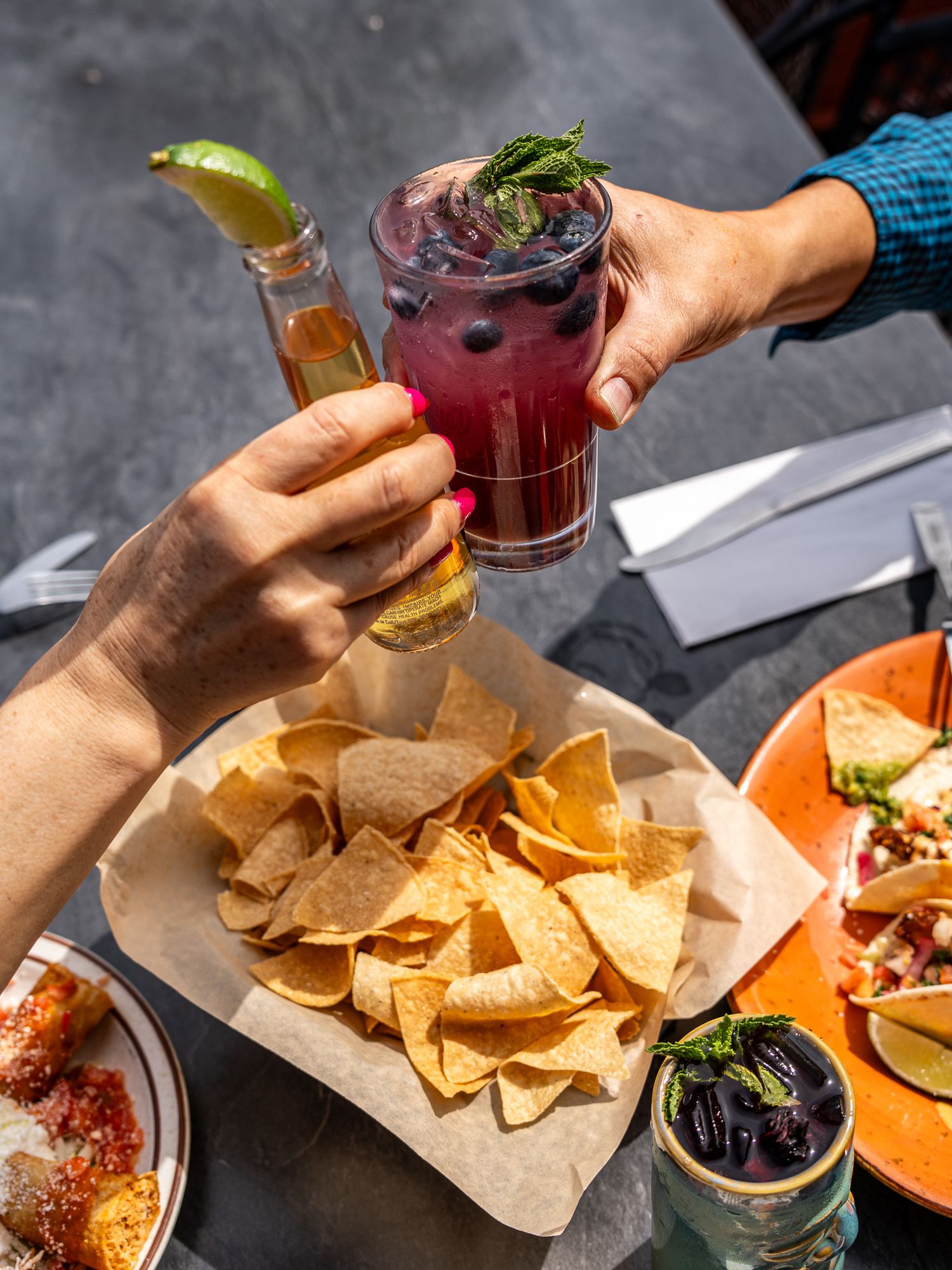 Hands toasting with beer and berry cocktail over basket of tortilla chips at restaurant.