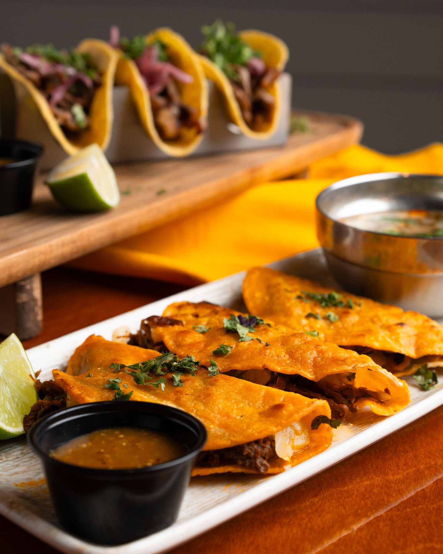 Mexican food platter with quesadillas and tacos served with dipping sauces and lime wedges.