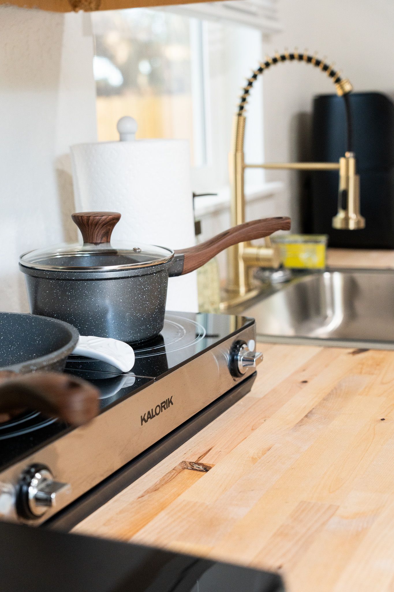 Modern kitchen countertop with black cookware and wooden cutting board on butcher block surface.