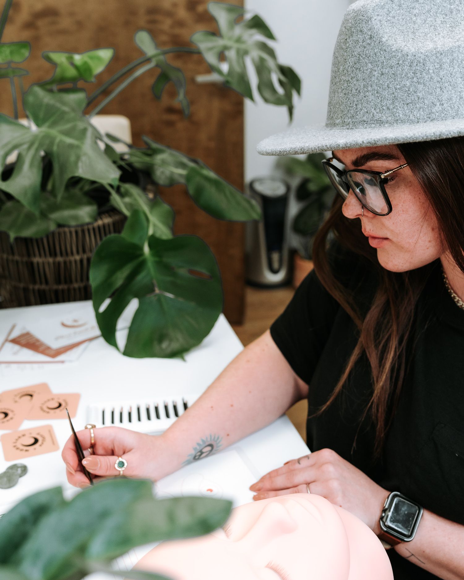 Lash technician working on client surrounded by indoor plants in modern salon setting.