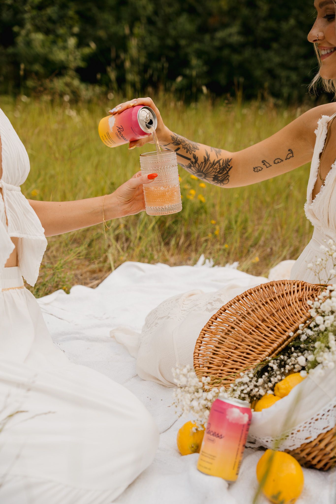 Picnic scene with white dress, wicker basket and colorful drinks on a blanket.