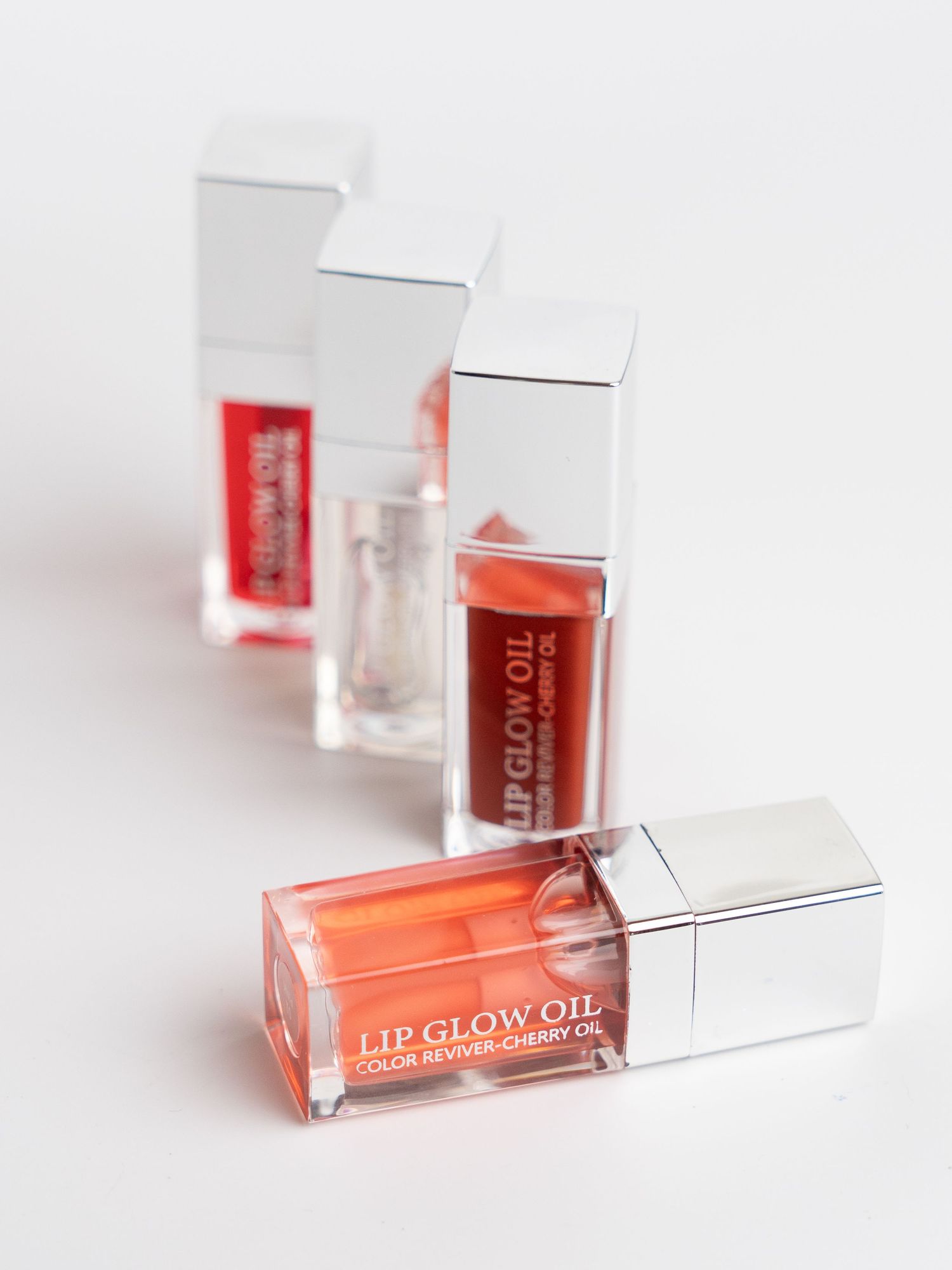 Coral-colored lip gloss bottles with clear applicators displayed on white background.