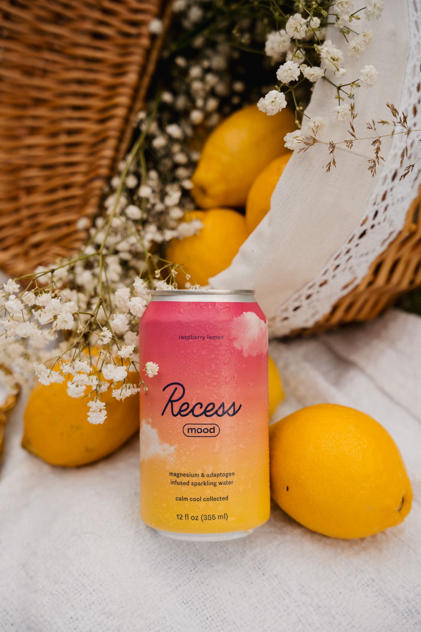 A pink Recess drink can placed near fresh lemons and delicate white baby's breath flowers in a rustic woven basket setting.