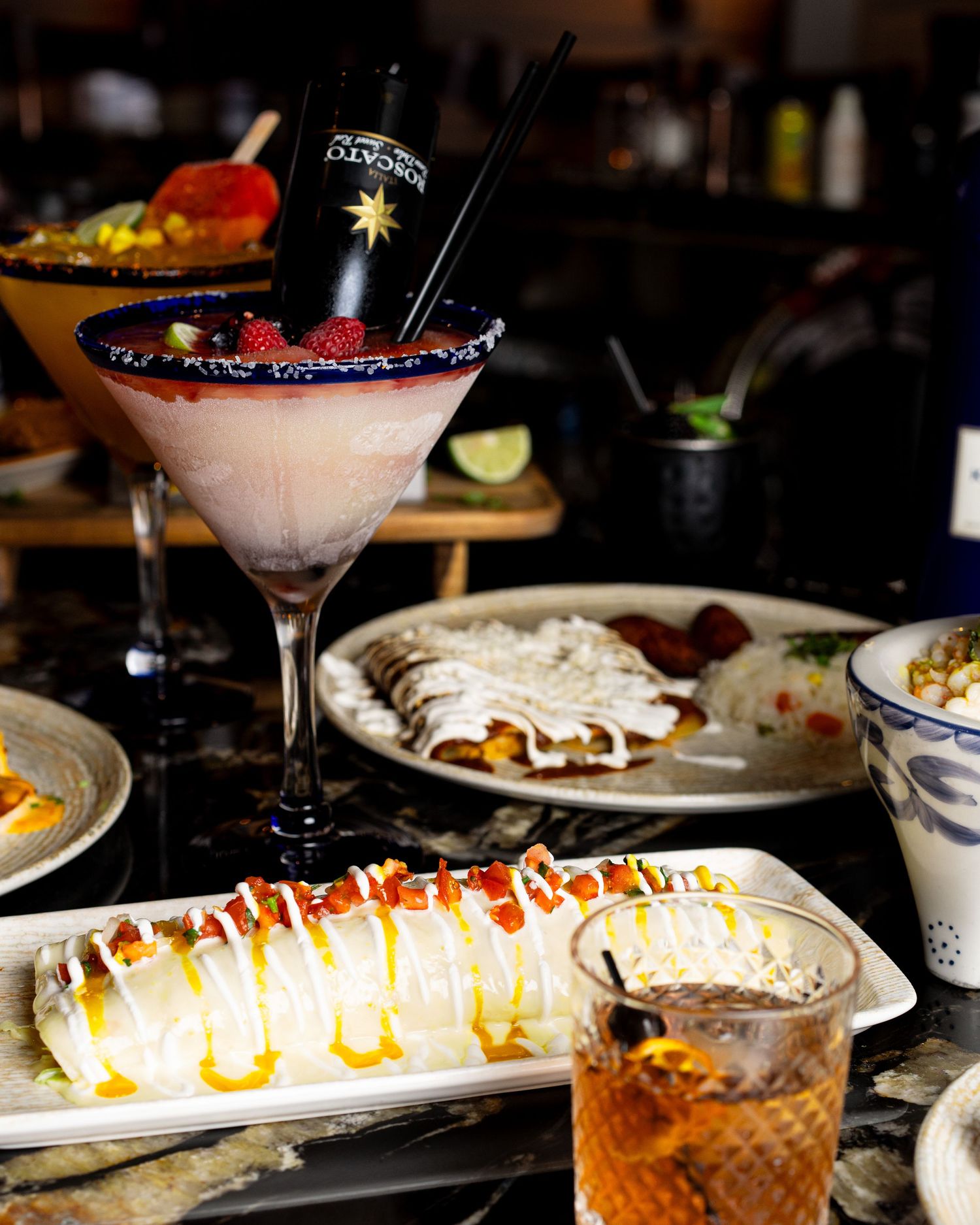 Elegant cocktail presentation with decorated martini glass and sushi rolls on a dark restaurant table.