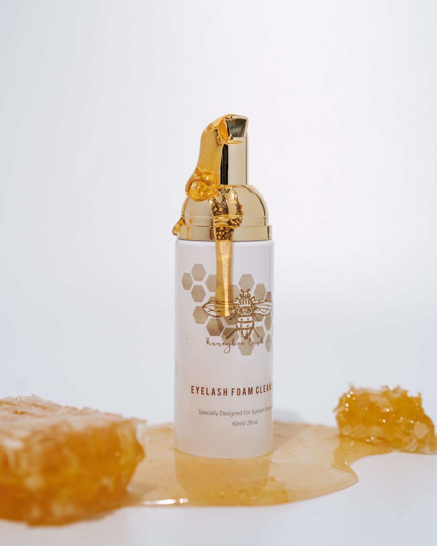 White cosmetic bottle with gold pump dispenser surrounded by honey crystals.