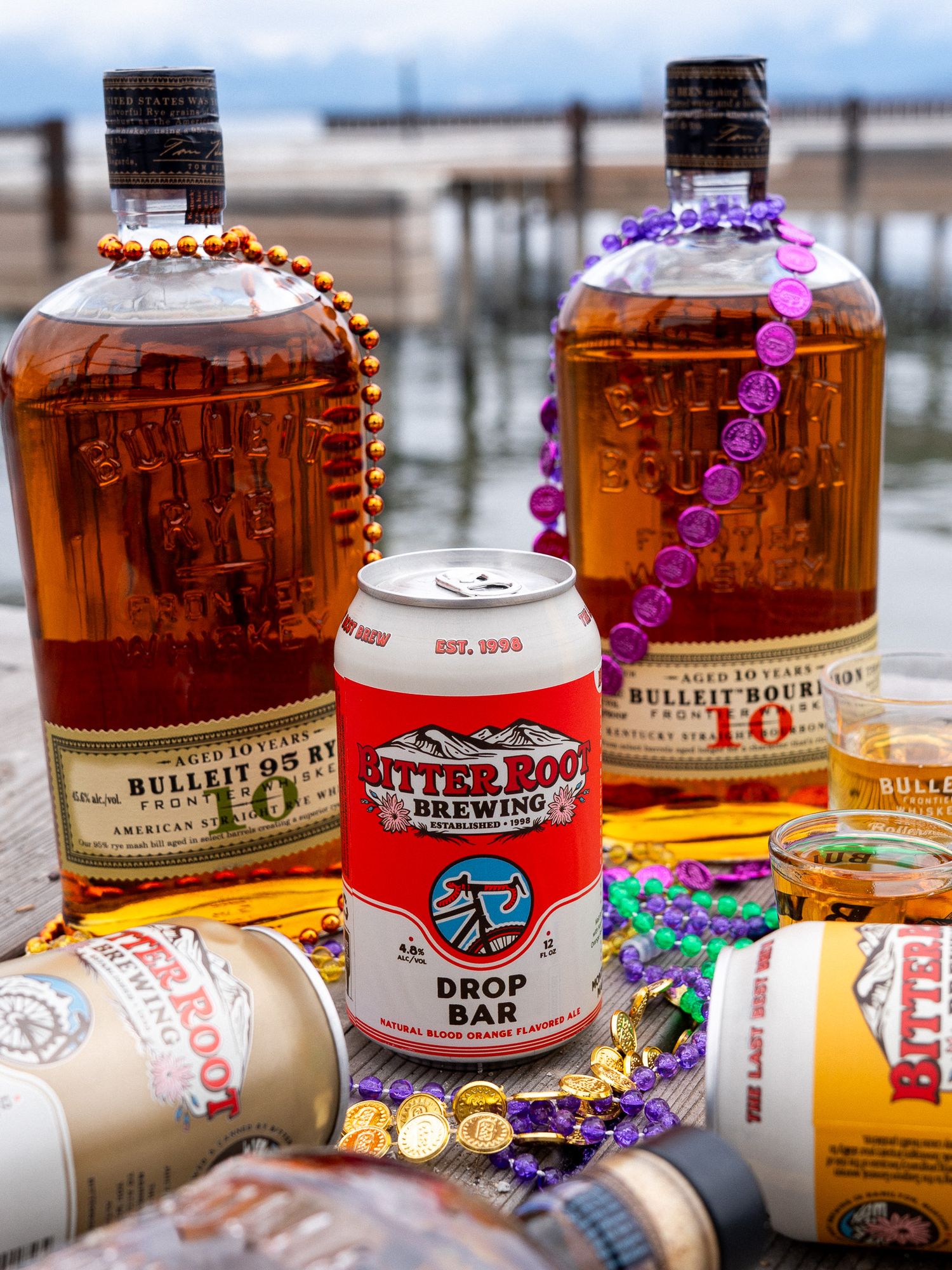 Bottles of Bulleit bourbon with Mardi Gras beads and canned cocktails arranged on outdoor deck.