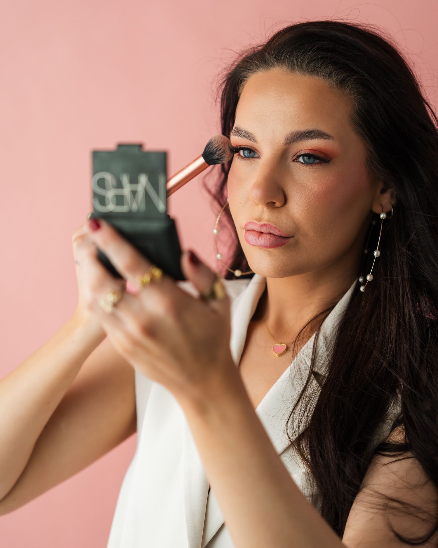 Close up shots of someone applying makeup with a phone against a pink background.