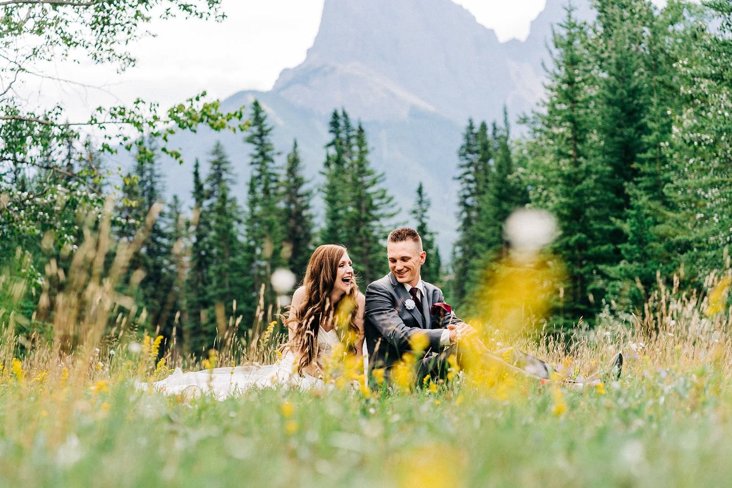 Couple sitting together in a lush mountain meadow with wildflowers and pine trees during their outdoor wedding.